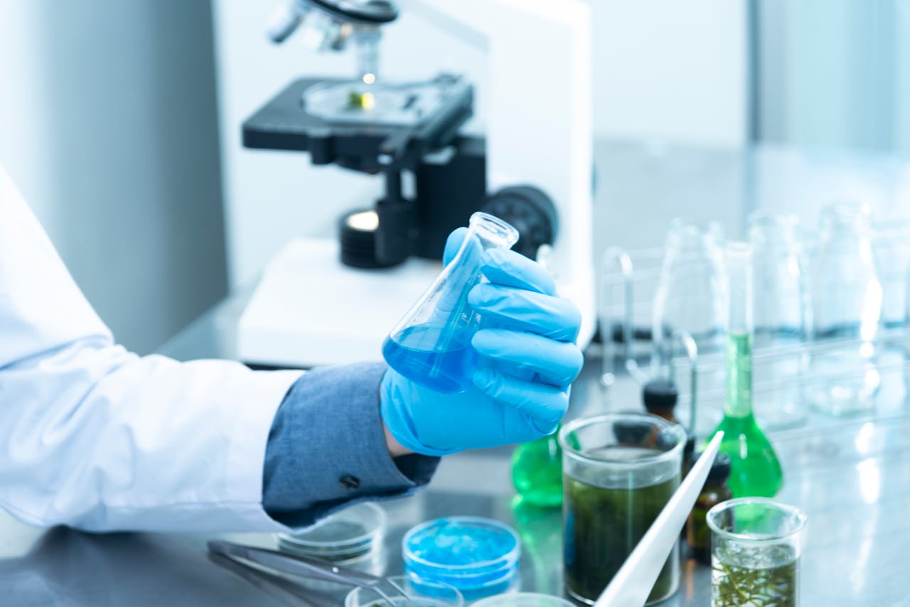 about-04 Scientist in gloves analyzing blue liquid in a laboratory setting with microscope and glassware.