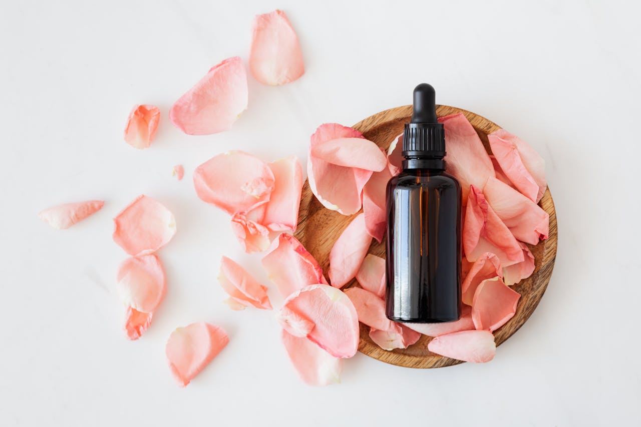 services-06 Top view of empty brown bottle for skin care product placed on wooden plate with fresh pink rose petals on white background isolated